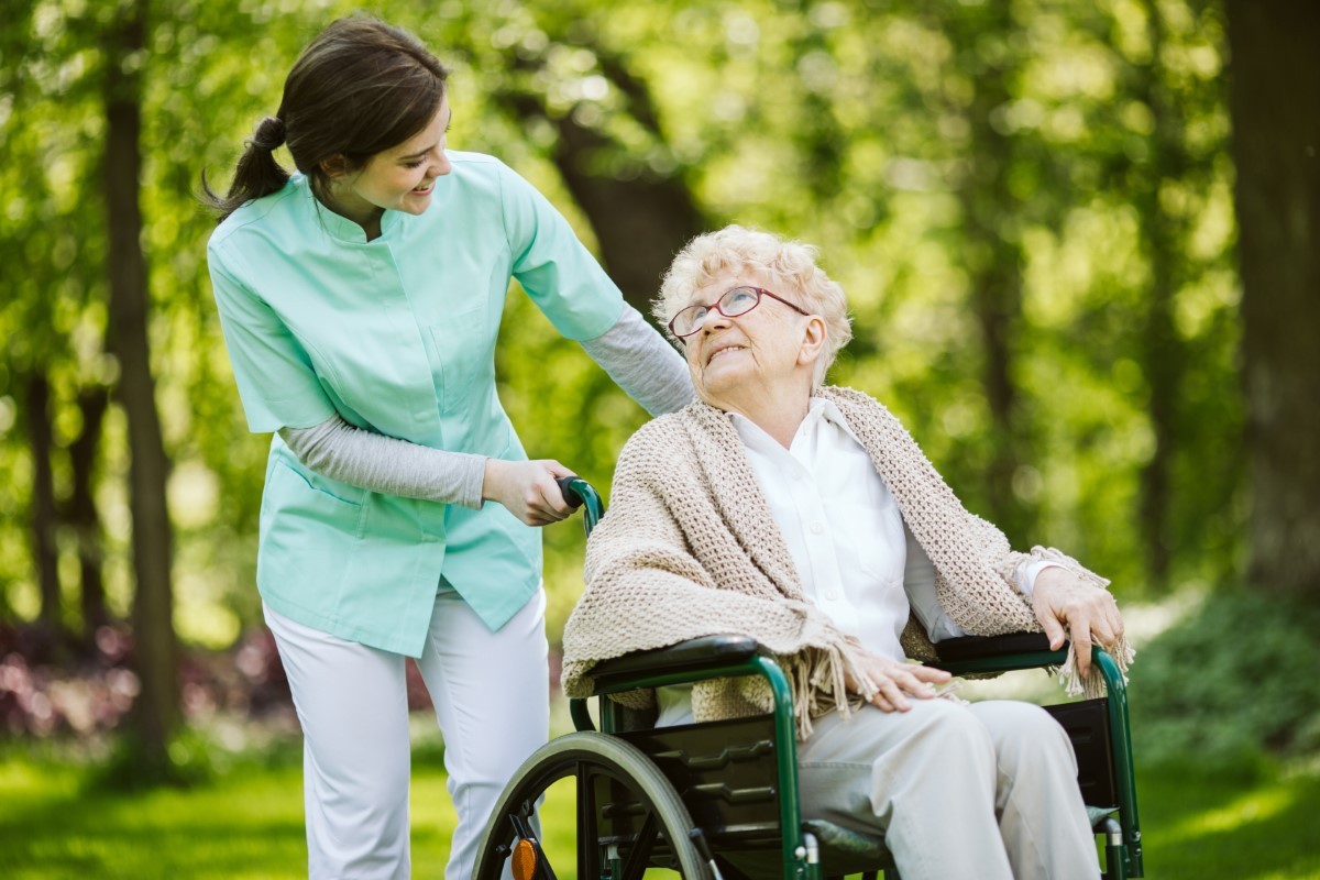 Senior disabled woman with caregiver in the garden of the nursing home